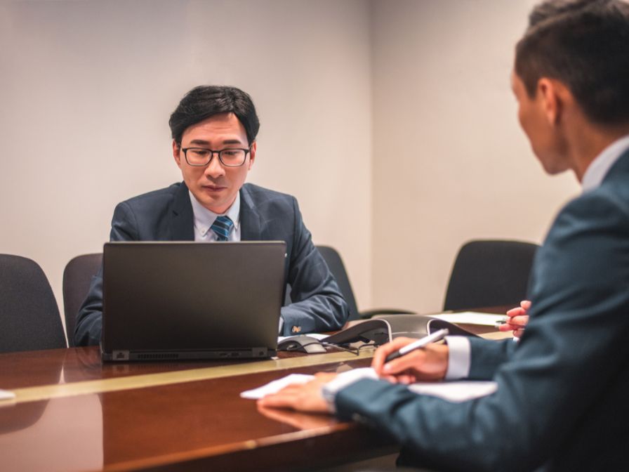 Two businessmen sitting at a desk work on a laptop